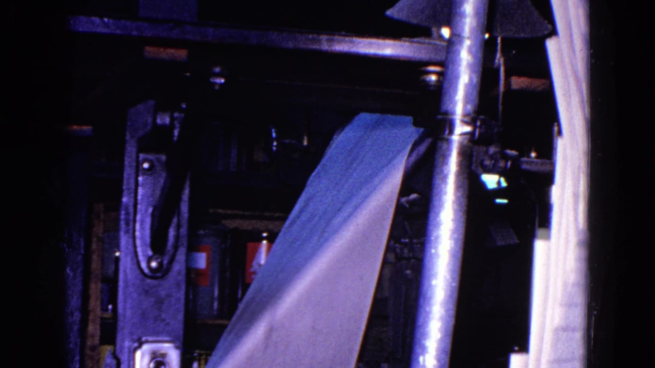 Printing press interior with angled paper sheet, metal uprights, rollers, and dark machine housing.