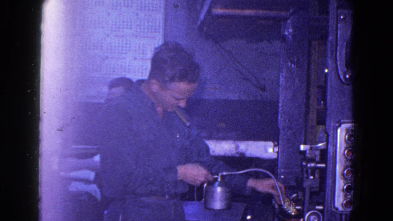 1967 Trenton 8mm frame showing a mechanic oiling a printing press with a metal oil can while smoking inside a dim industrial room.