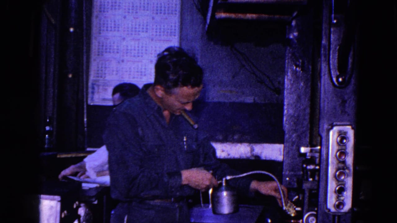 1967 Trenton 8mm frame of a worker beside press controls, using an oil can near the machine with a wall calendar behind him.