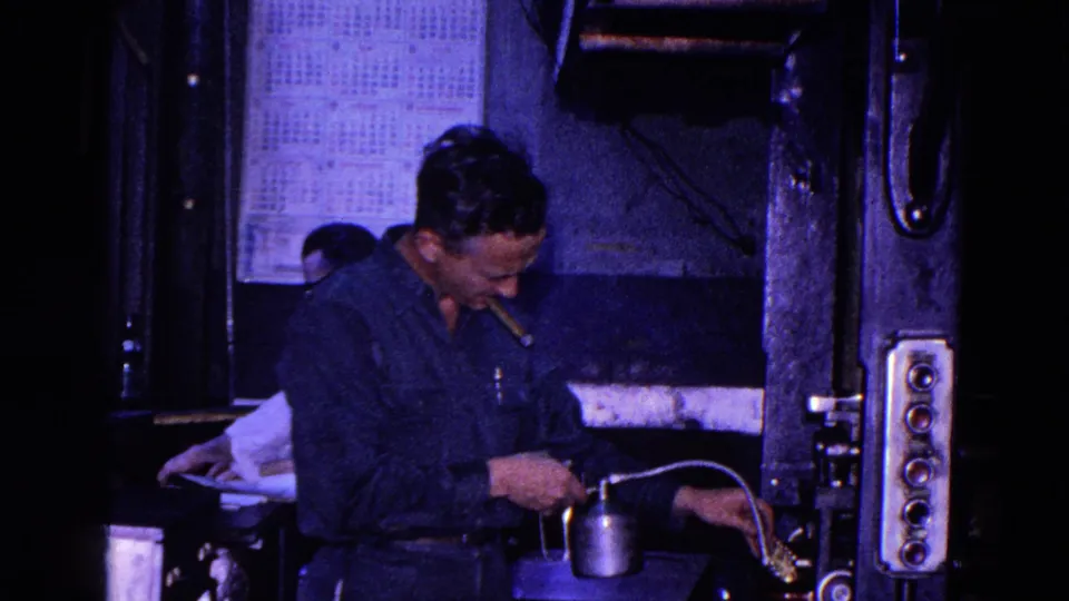 1967 Trenton 8mm frame of a worker beside press controls, using an oil can near the machine with a wall calendar behind him.