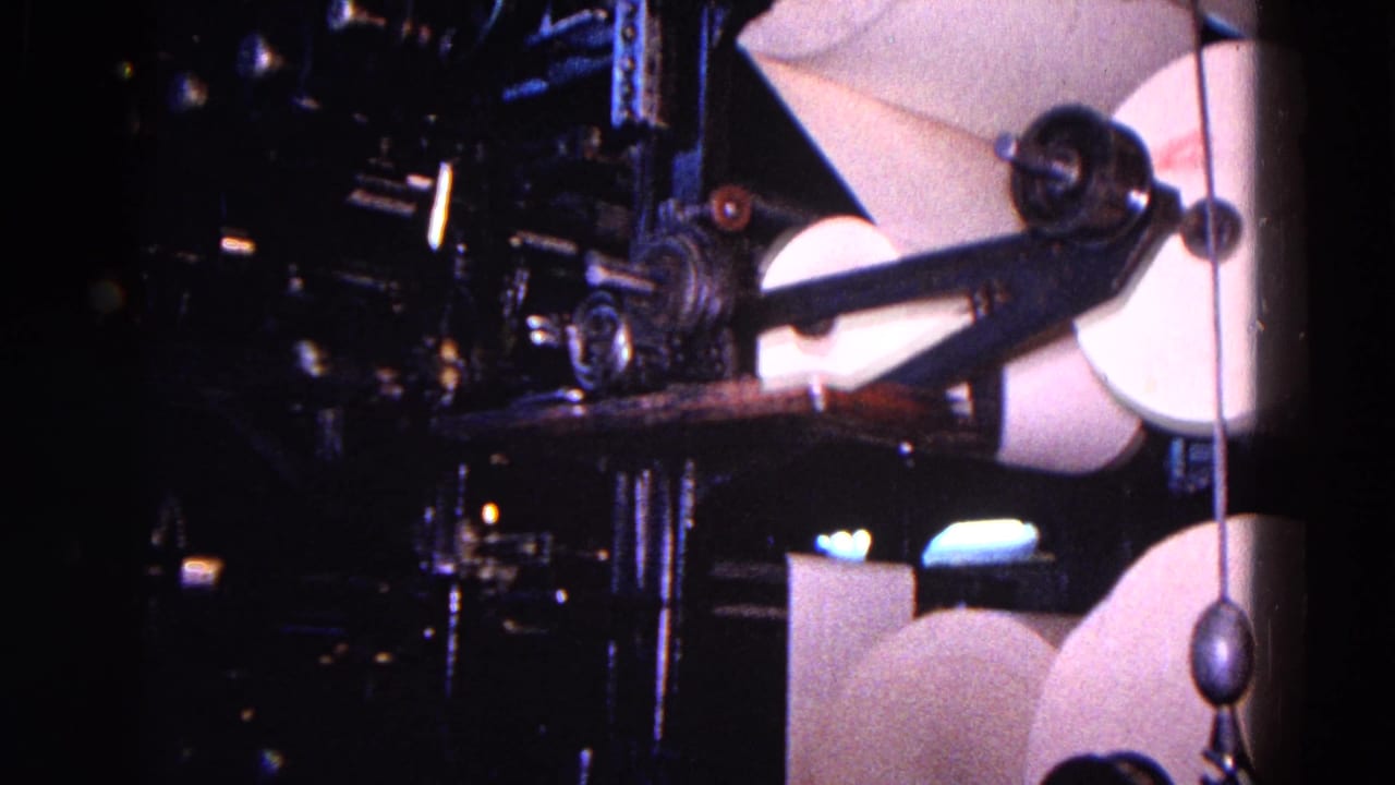Paper reels and press rollers dominate the frame in this 1967 Trenton industrial printing scene, with dark machine parts and a hanging counterweight visible.