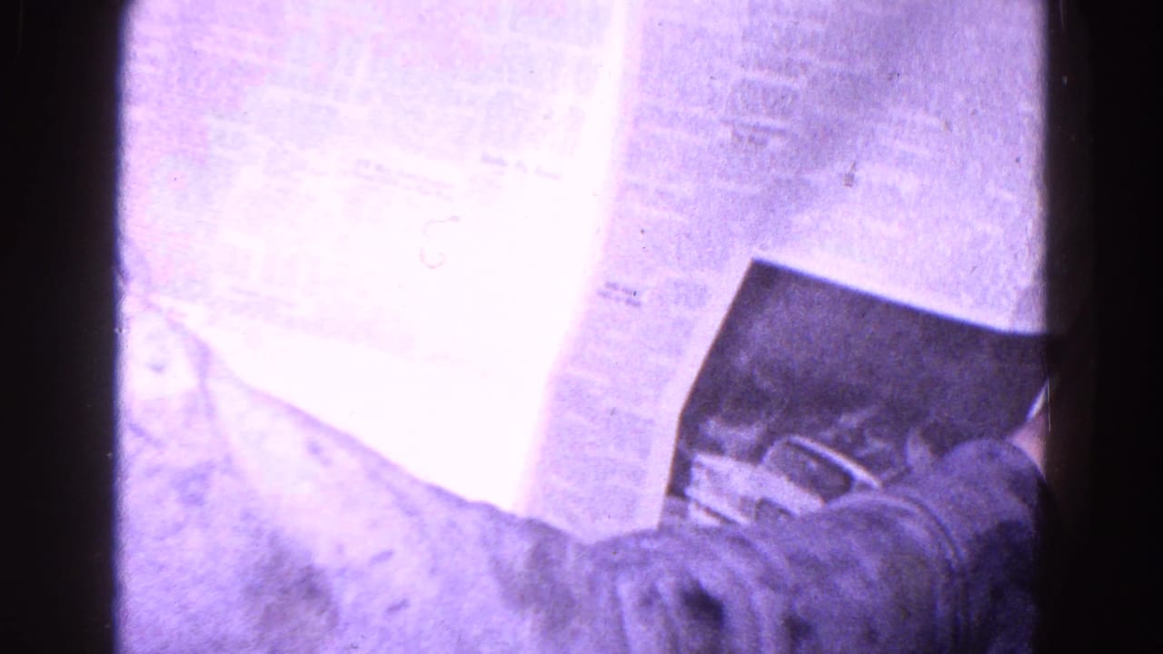 Printed newspaper sheets held close to the camera, with a sleeve and hand partly visible.
