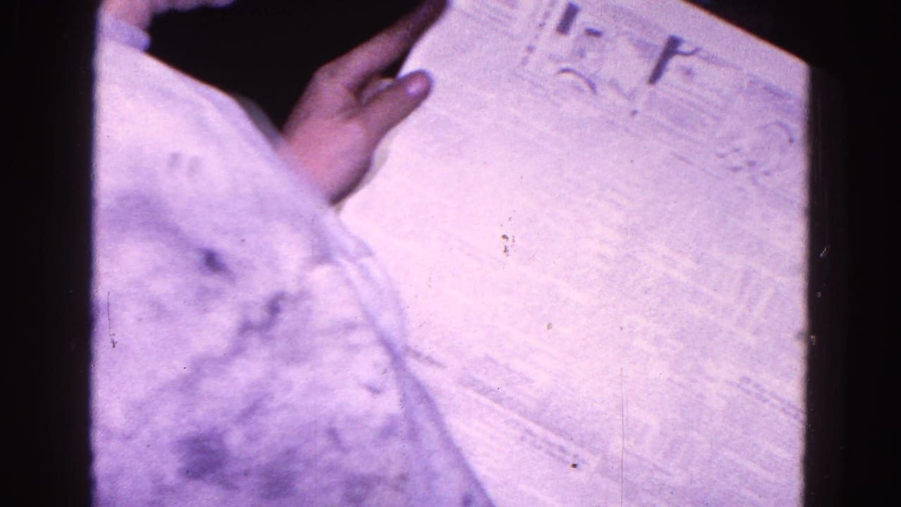 1967 Trenton 8mm frame showing a hand examining a printed newspaper page near the end of the clip.