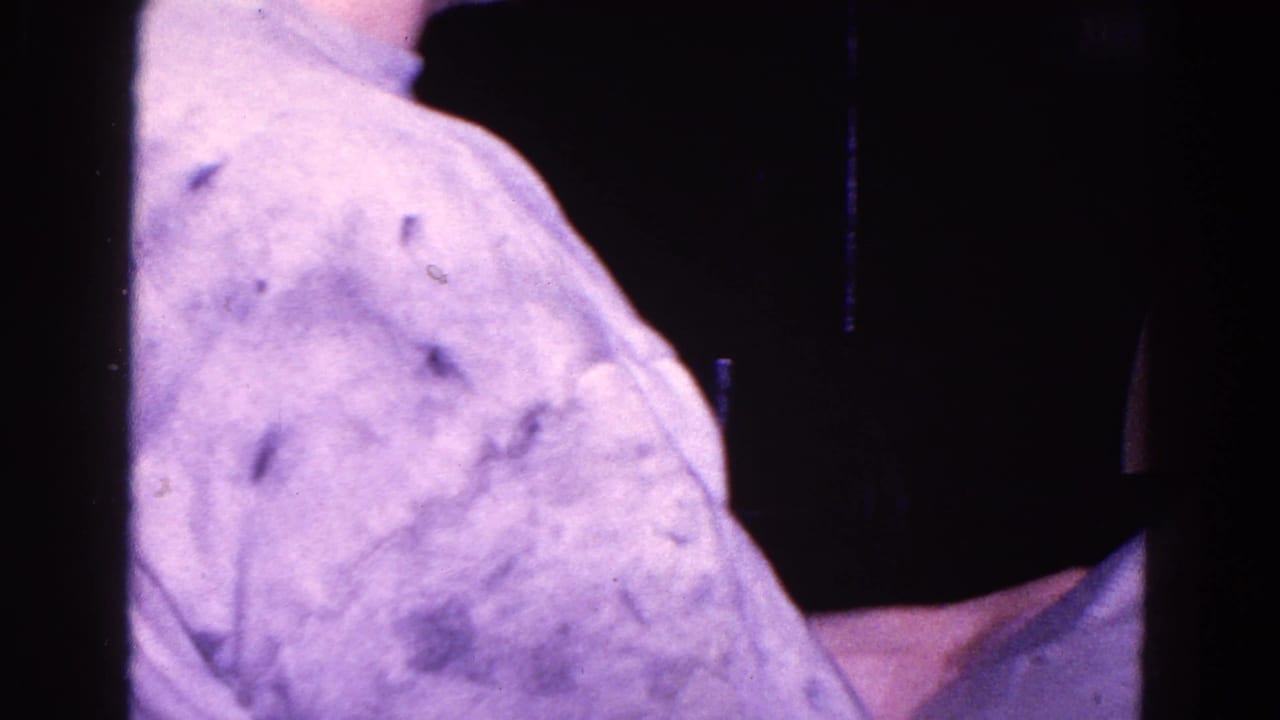 Close view of a man in a light patterned shirt holding a newspaper in a dark room.