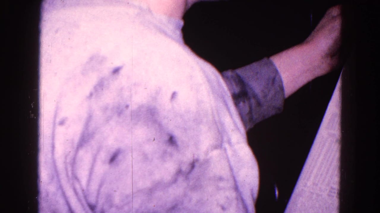 A man in a light shirt reaches across a dark interior while holding or turning a newspaper.