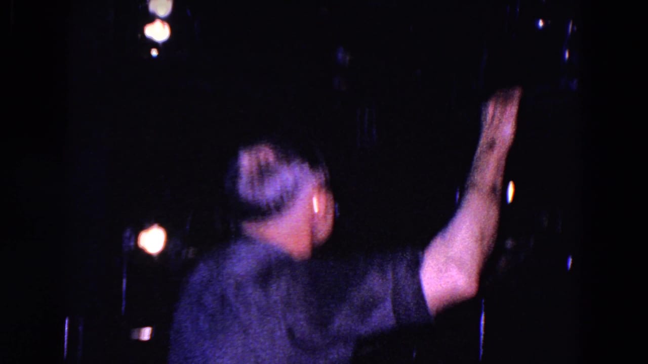 Man reaches toward dark projection equipment in a booth.