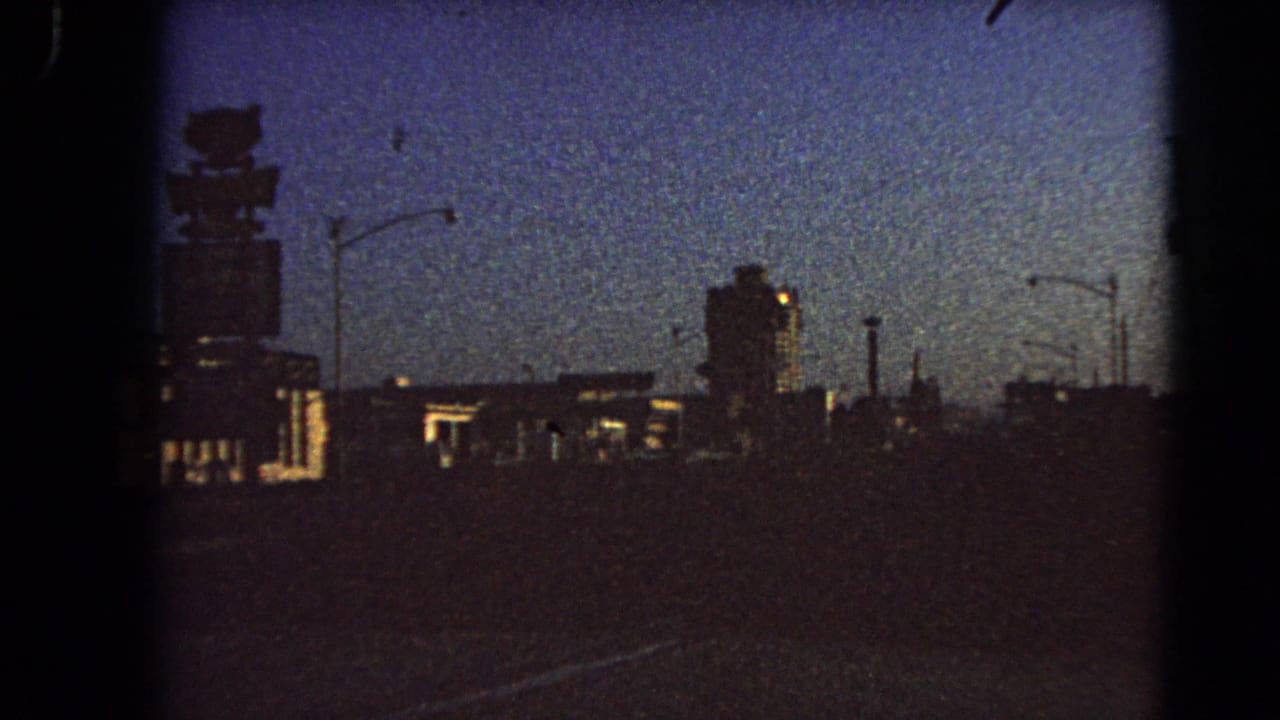 Twilight street view with a large rooftop sign silhouette, dark buildings, and streetlights.