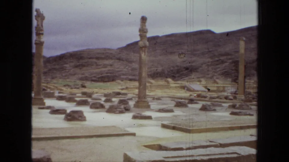 1972 Iran 8mm frame showing upright stone columns, scattered blocks, and arid hills at an archaeological site.
