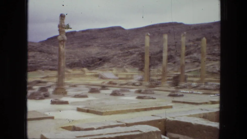 1972 Iran 8mm frame with multiple standing columns, broken masonry, low platforms, and dry hills behind the site.