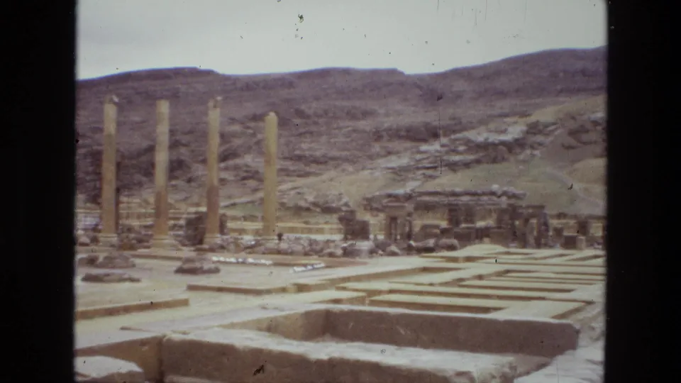 1972 Iran 8mm frame showing tall columns, rectangular stone foundations, scattered ruins, and arid hills in the background.