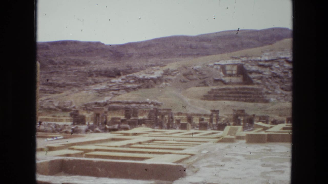 1972 8mm frame of Persepolis in Iran with low stone foundations, column remains, and a sloping hillside behind the site.