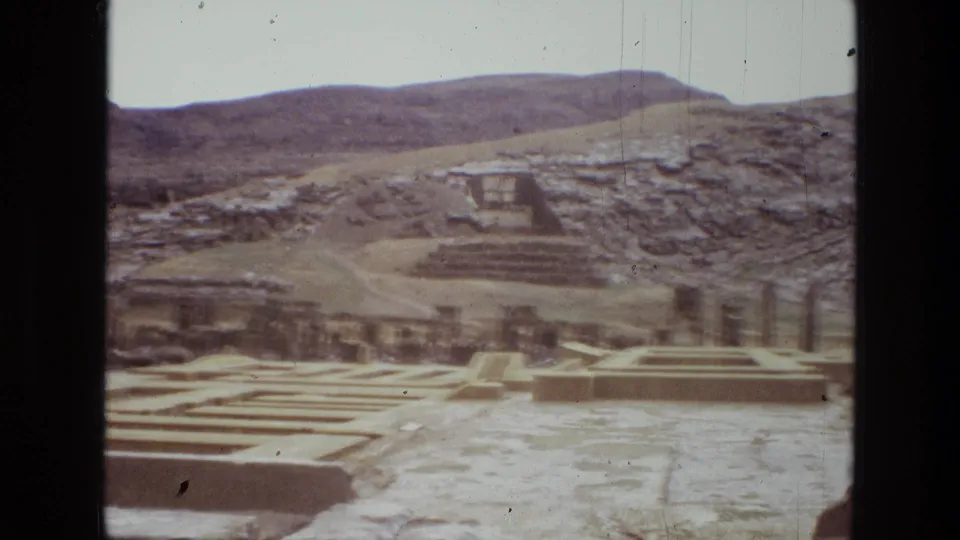 1972 8mm view across Persepolis ruins in Iran, with stepped platforms, broken stonework, and rocky hills beyond.