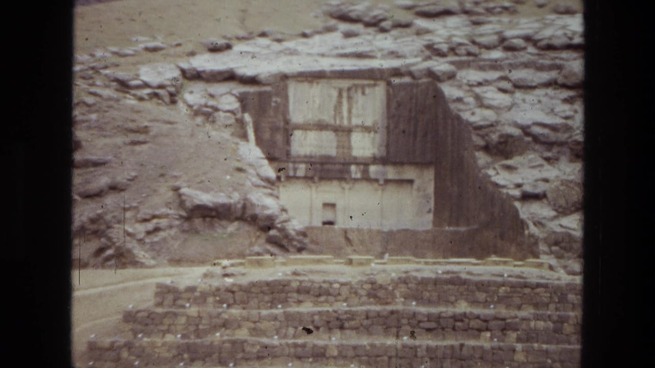 1972 Iran travel footage frame showing a weathered stone facade, hillside rock, and stepped masonry in the foreground.