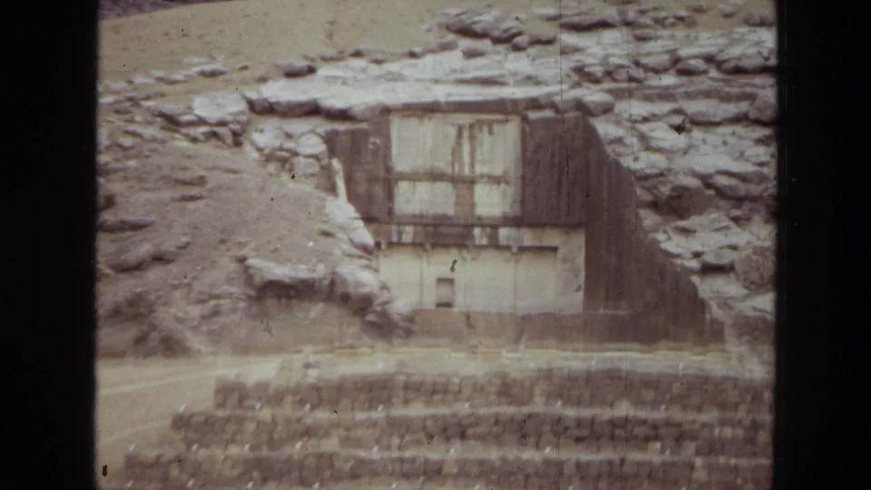 Handheld 1972 8mm frame from Iran with a closer view of the hillside structure and layered stone platforms below.