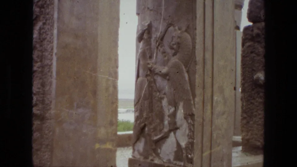 1972 Iran 8mm frame showing a carved bas-relief figure on stone, framed by vertical architectural surfaces at the ruin site.