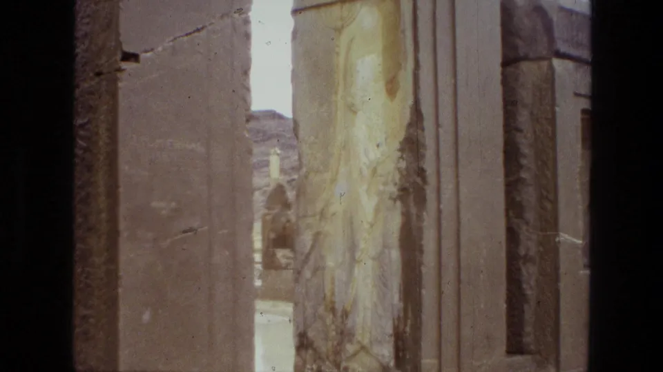 1972 Iran 8mm frame looking past worn stone surfaces and columns toward a narrow opening inside an archaeological ruin.