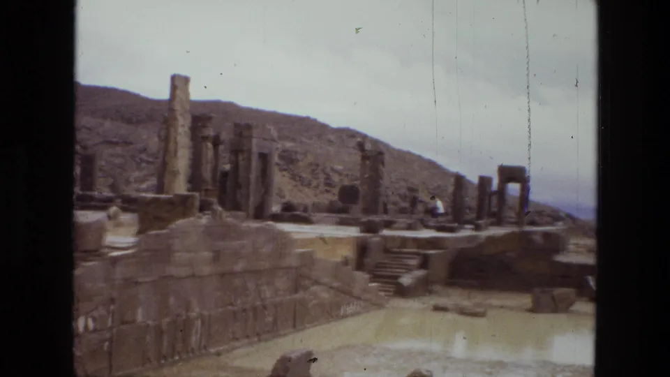 1972 8mm view of ancient ruins in Iran, with standing columns, stone terraces, steps, and a reflective muddy pool.