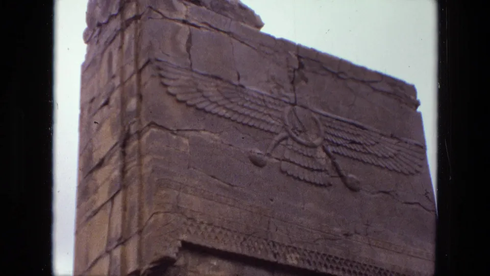 1972 Iran 8mm frame with an angled visitor view of a winged carving across cracked, weathered stone.