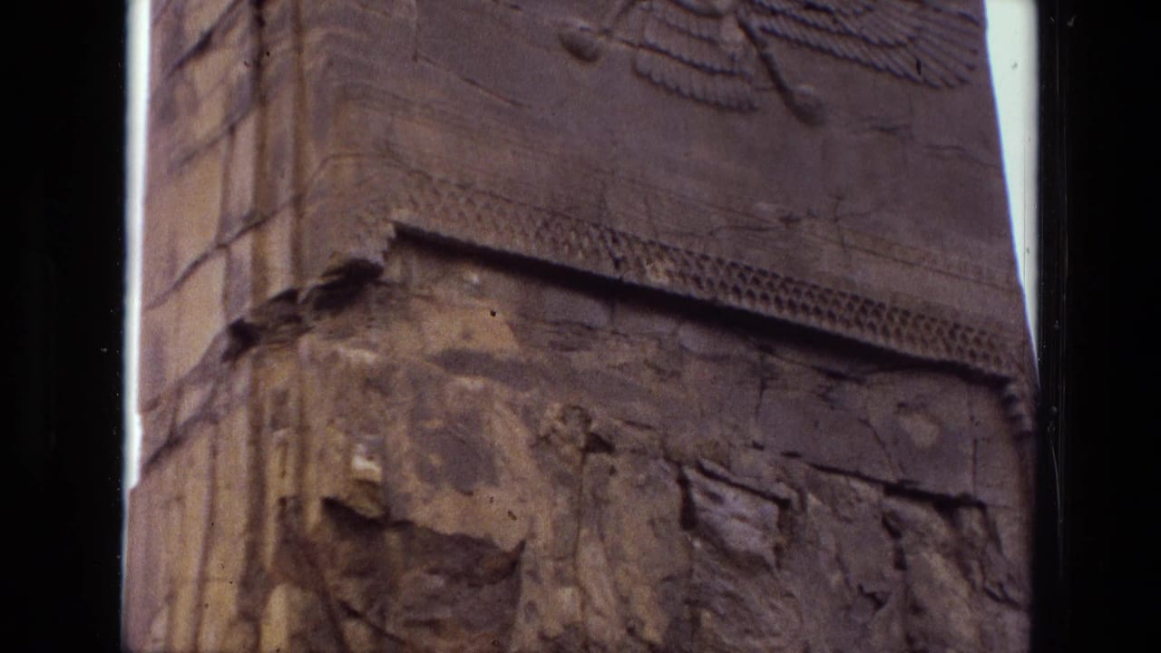 Weathered stone relief with a winged emblem near the top and damaged carved figures below.