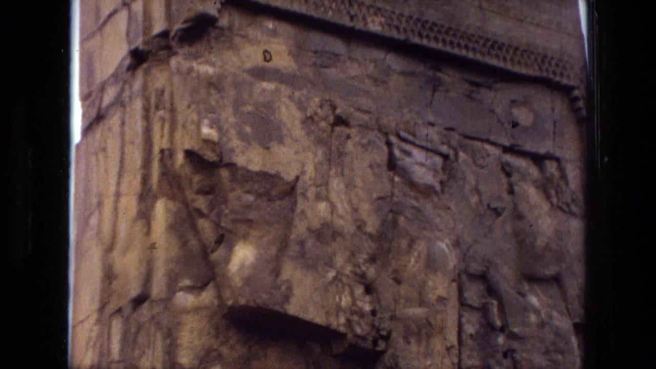 Close view of damaged stone carvings with eroded relief forms and a winged motif at the edge.