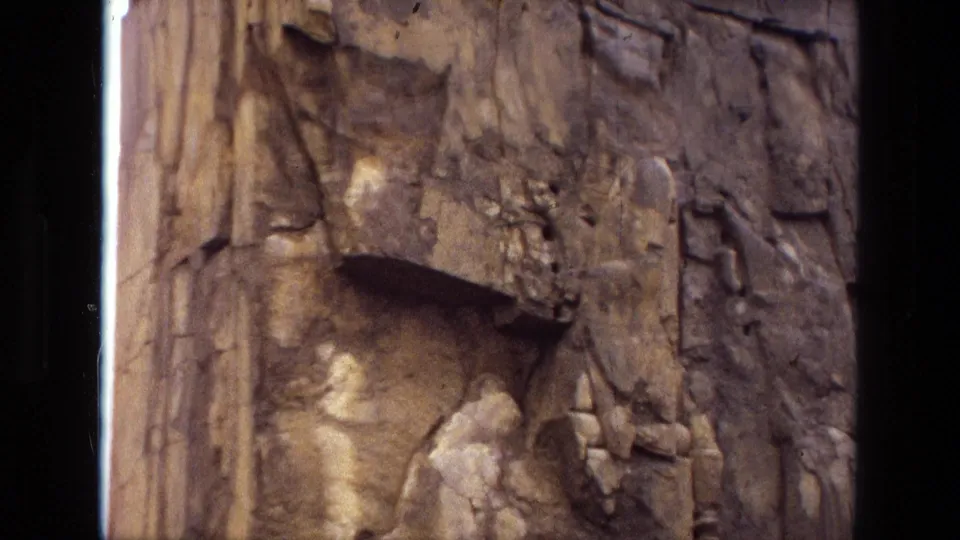 1972 8mm Iran frame showing the lower portion of an ancient-looking stone relief with broken figures, cracks, and worn pale surfaces.