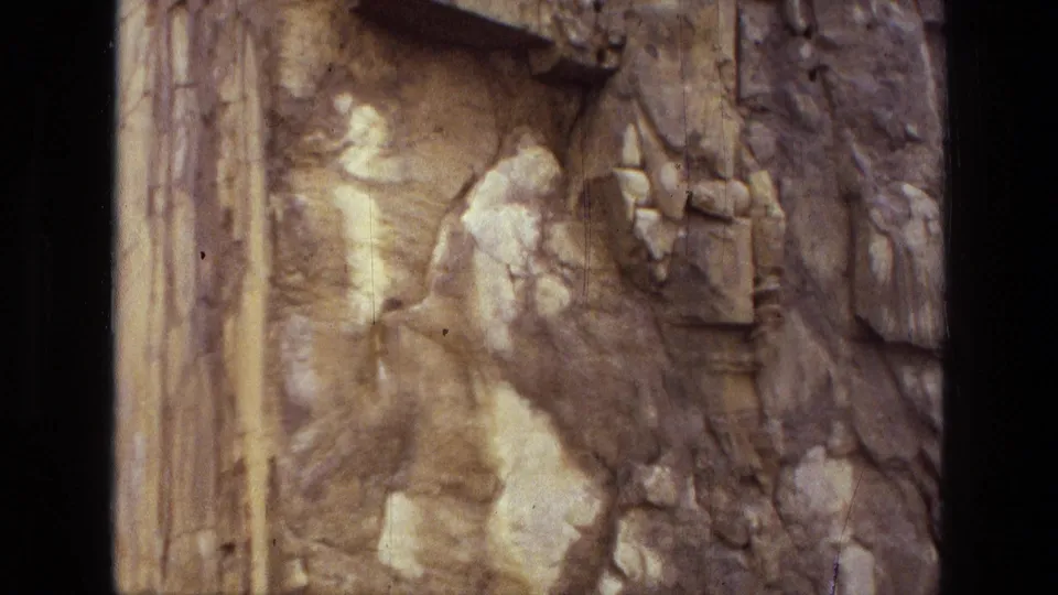 1972 Iran 8mm frame showing a weathered bas-relief surface with fractured figures, eroded patches, and visible film-frame borders.