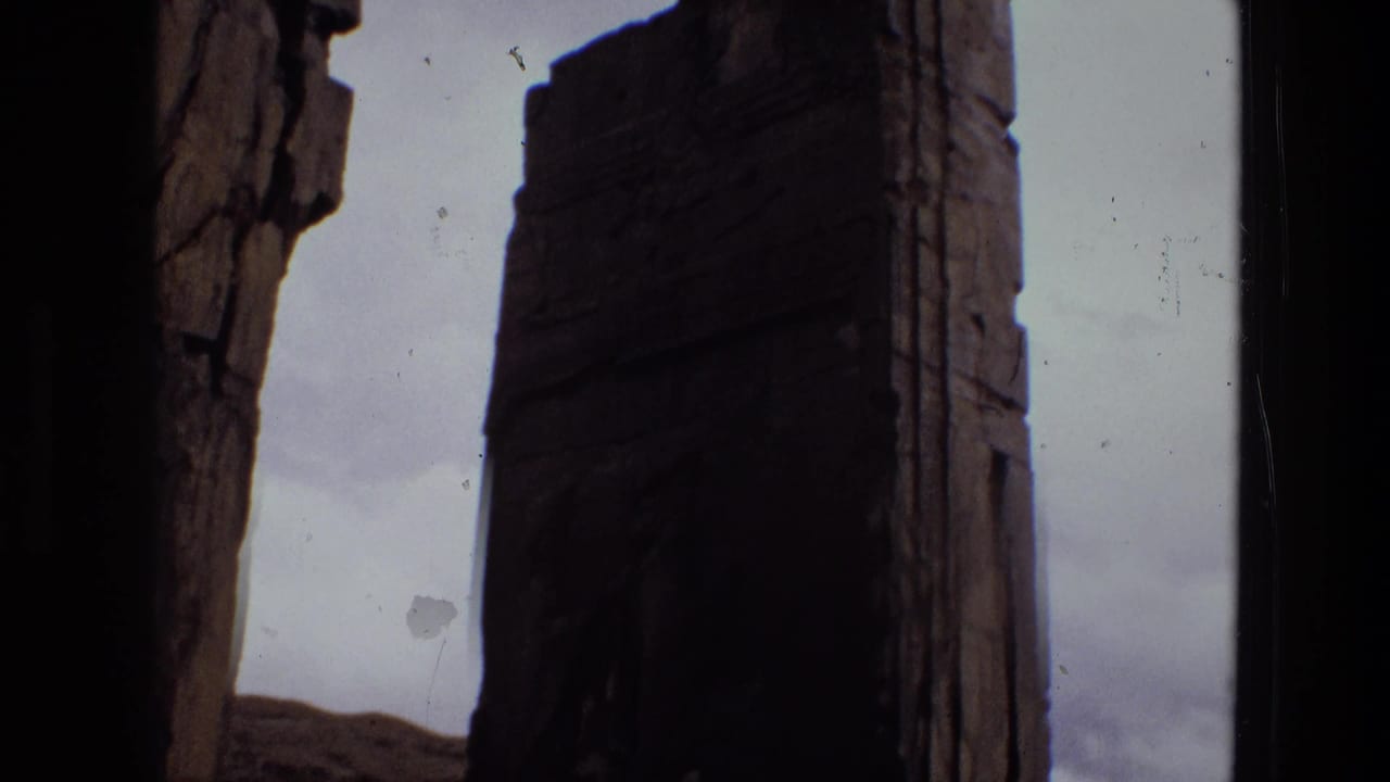 Tall dark stone column seen against a pale sky and rocky ground.