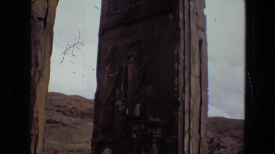 1972 Iran 8mm frame showing a shadowed carved pillar between stone edges, with barren hills and pale sky in the background.