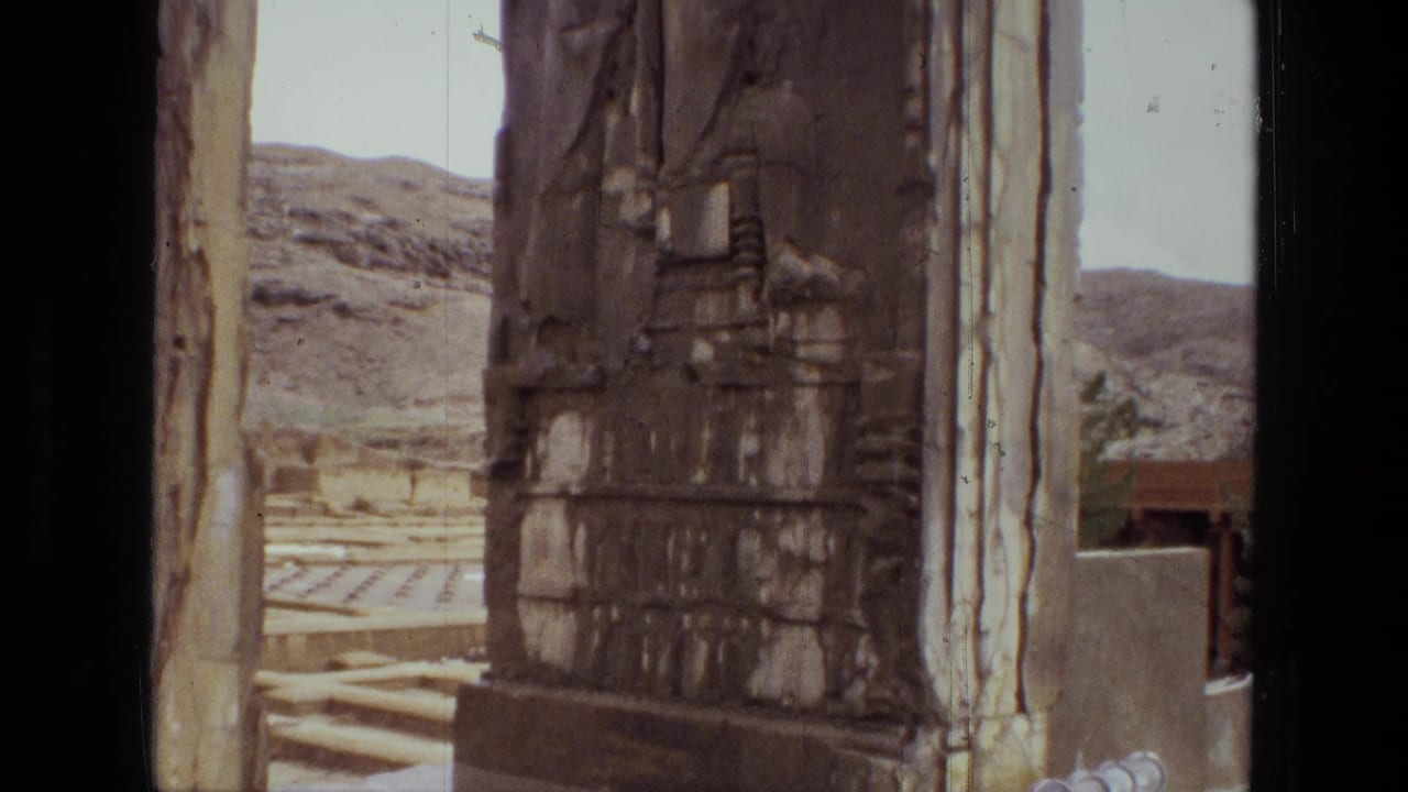 Carved stone pillar seen through a tall opening with hills and ruins behind it.