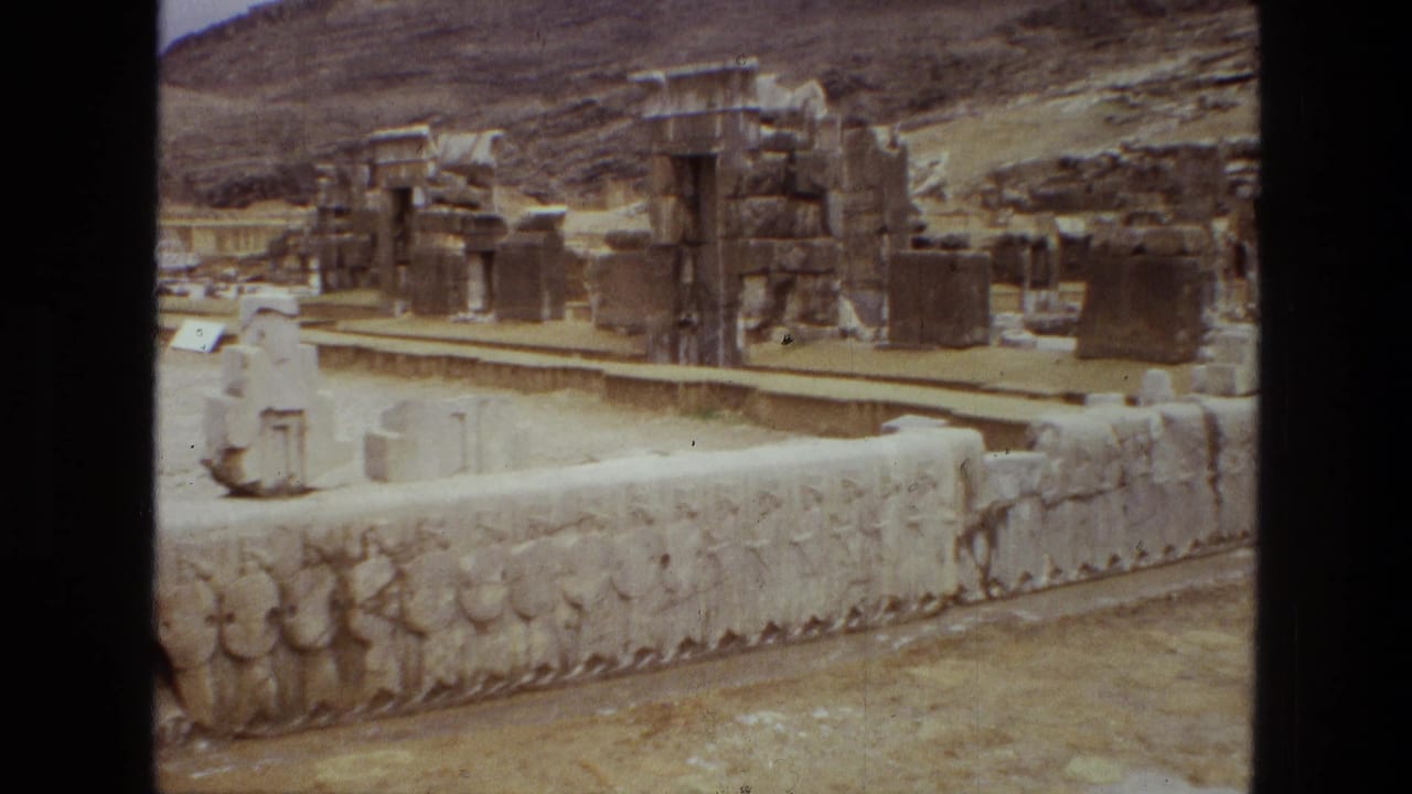 Tan stone ruins and a carved wall below rocky hills.