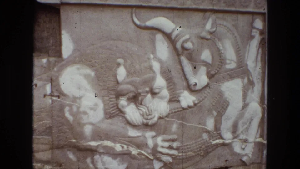 1972 Iran home-movie frame showing pale carved relief panels with horned animals, figures, and mythological forms in soft faded color.