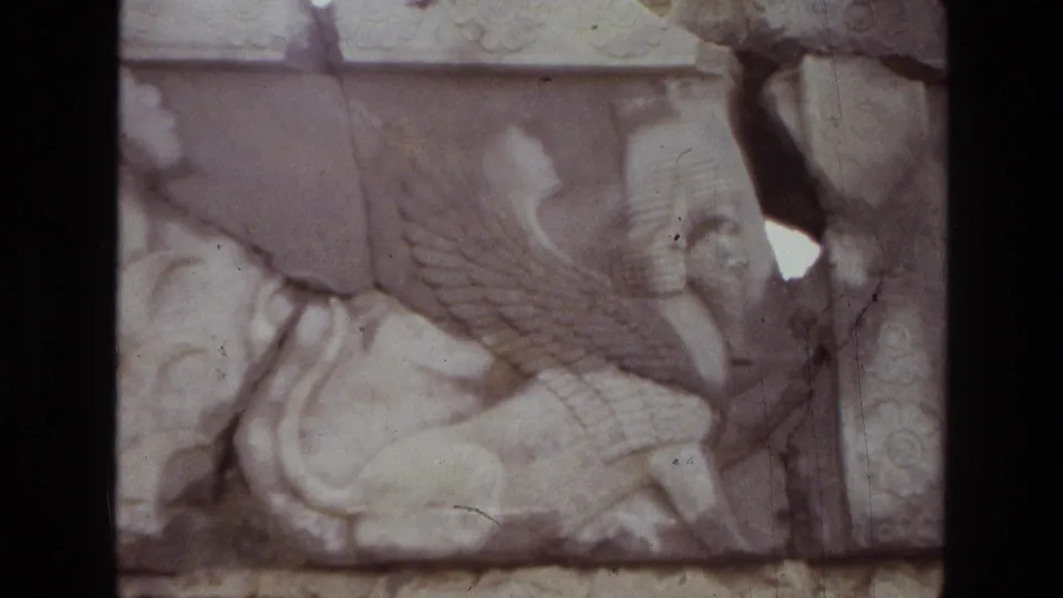 1972 Iran frame with a close view of a pale stone winged creature relief, framed by dark film edges and visible film wear.