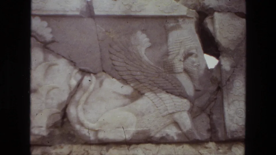 1972 Iran home-movie close-up of a weathered winged creature relief, with soft focus, faded color, and dust marks on the film.