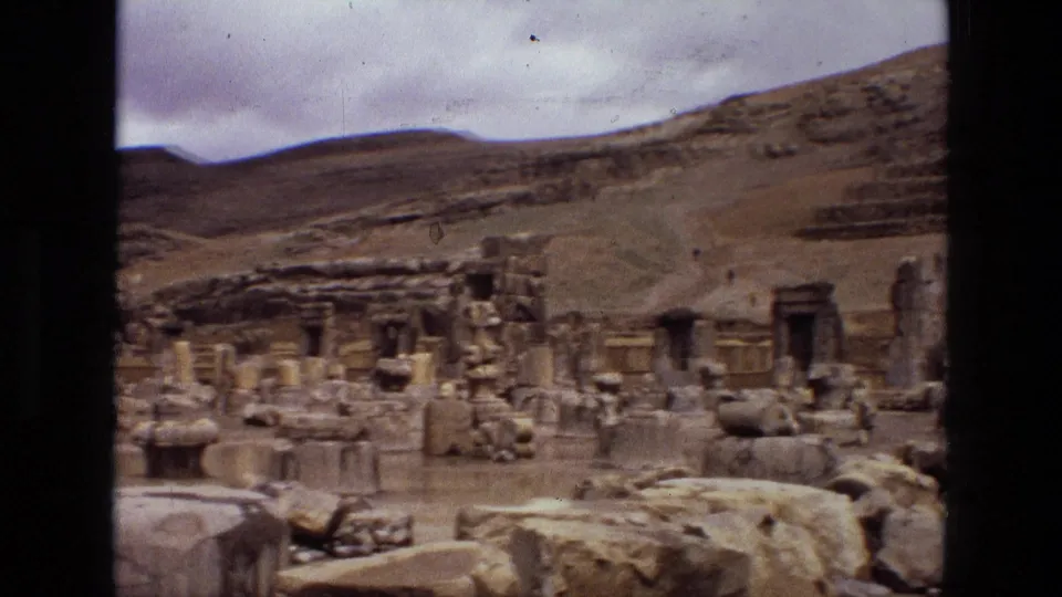 Handheld 8mm view across an Iranian ruin site in 1972, showing broken masonry, scattered blocks, and a sloping landscape behind the remains.