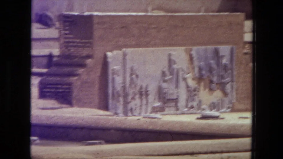 Close 1972 Iran 8mm view of a carved stone relief panel at the ruin site, with adjacent blocks and soft film color fading visible.