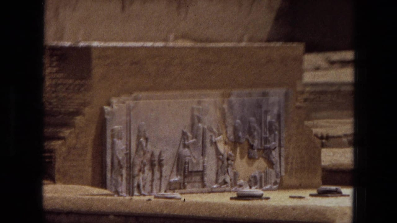 Carved stone relief panel mounted on a sandy exterior wall, partly framed by dark vertical edges.