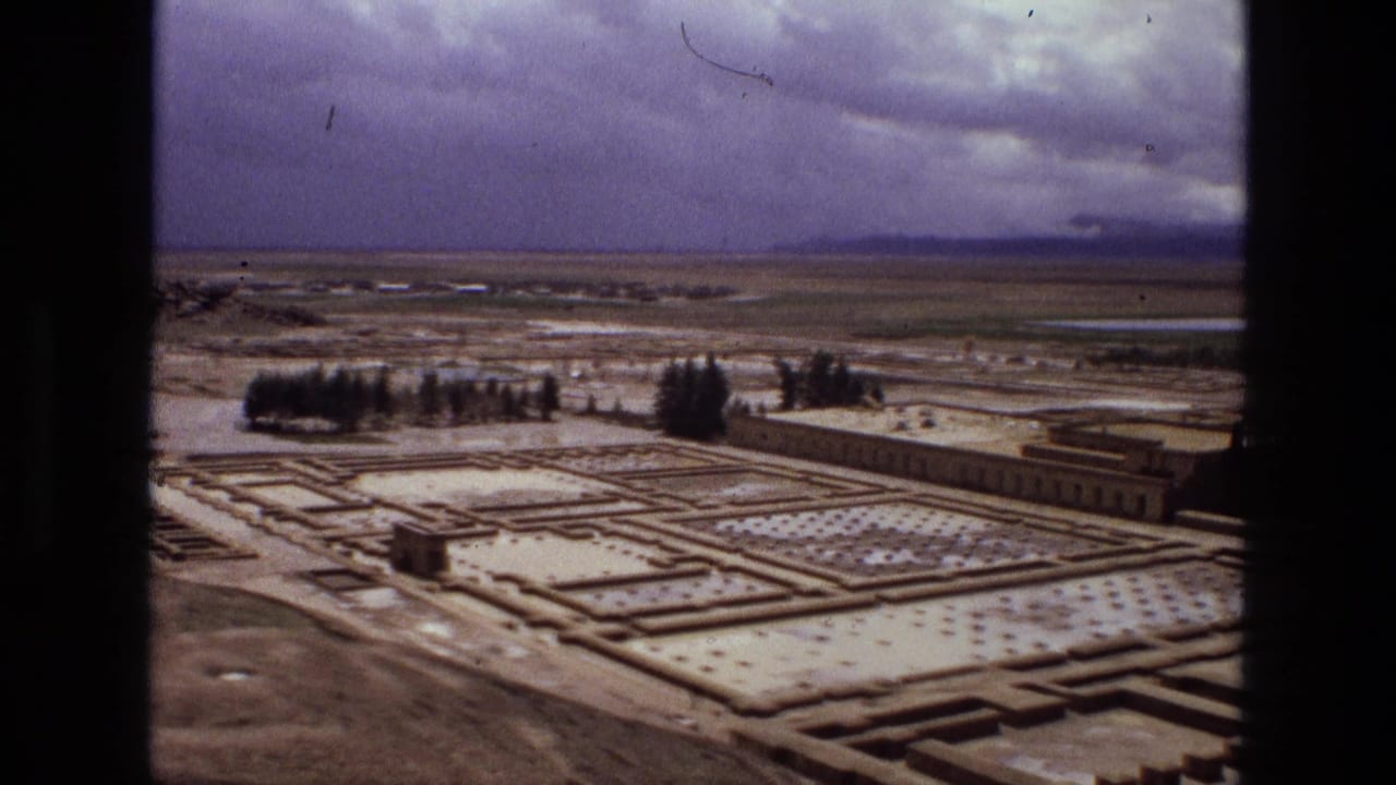 1972 Iran 8mm frame showing an elevated view across rectangular garden beds, low stone paths, scattered trees, and distant flat fields.