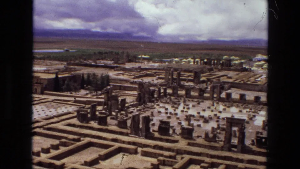 Final 1972 Iran frame showing a wider portion of the geometric site, with low garden divisions, upright stone elements, trees, and an overcast horizon.