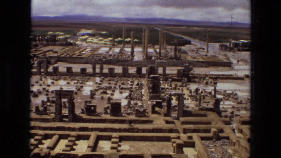 1972 8mm aerial view in Iran showing an ancient ruin field, upright columns, foundations, and access paths.