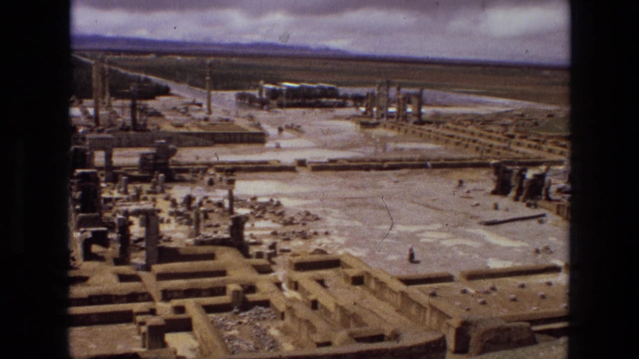 Aerial view over desert ruins with stone foundations and standing columns under a cloudy sky.