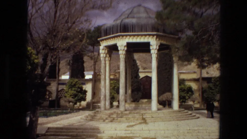 1972 Iran travel footage frame showing a columned garden pavilion with stone steps, trees, and a small indistinct person nearby.