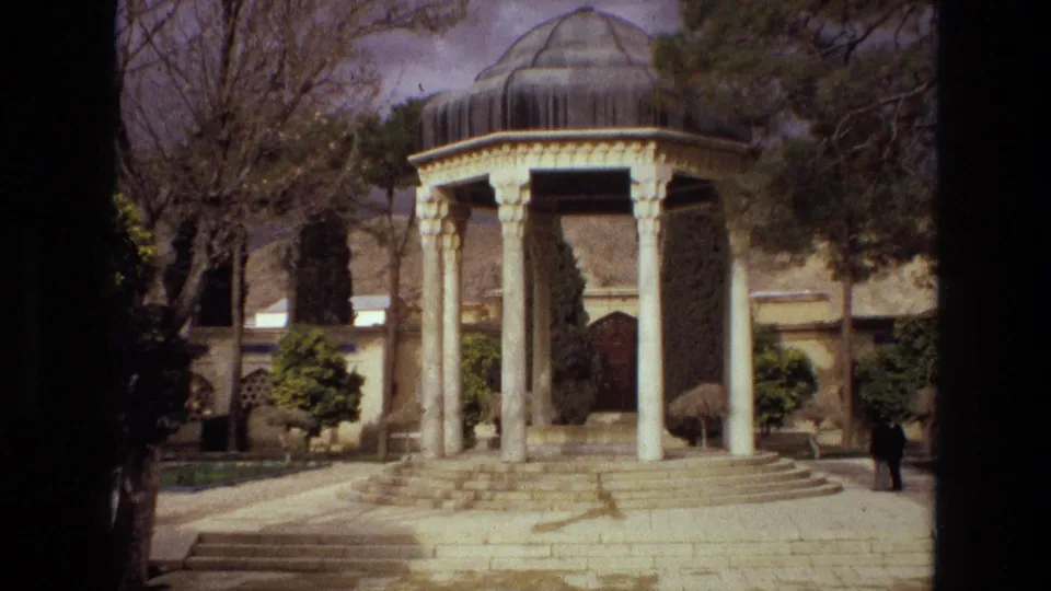 1972 Iran 8mm frame showing a domed Persian-style pavilion on stone steps, with trees, shrubs, and a small visitor nearby.