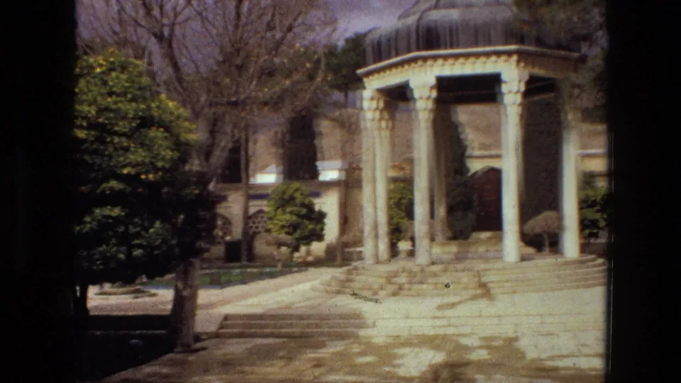 1972 Iran 8mm view of a domed pavilion in a garden, with a tree trunk and shaded foliage partly blocking the frame.