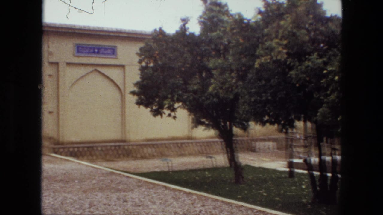Courtyard with trees, gravel paths and a pale arched building wall.