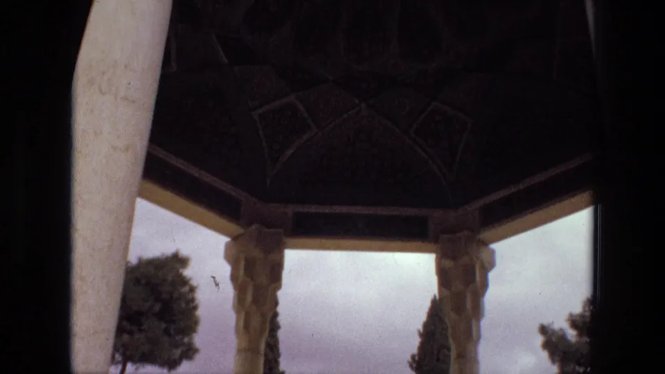 1972 Iran 8mm frame looking from a shaded pavilion through ornate columns toward trees and an overcast garden.