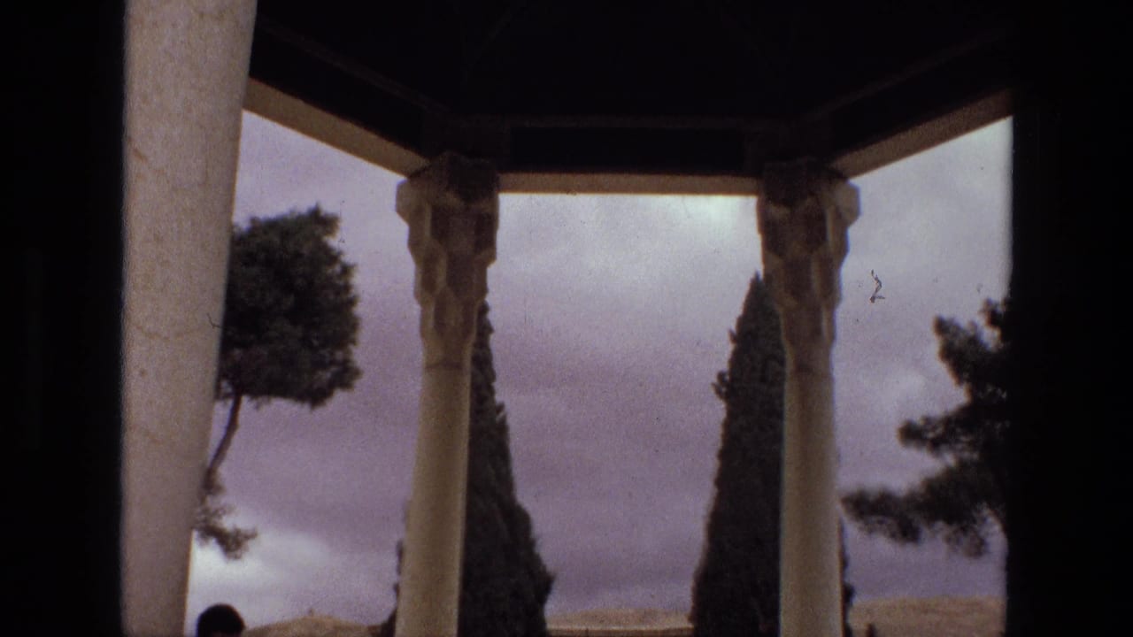 1972 Iran home-movie view through pale pavilion columns toward trees, sky, and a partially visible person below.