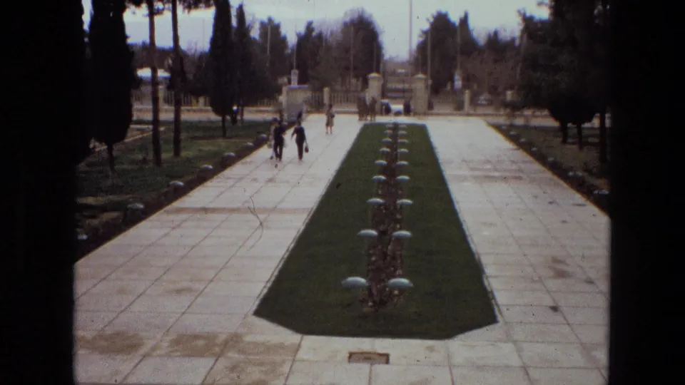 1972 Iran frame showing people walking along white tiled garden paths beside a long central lawn strip and rows of low plantings.