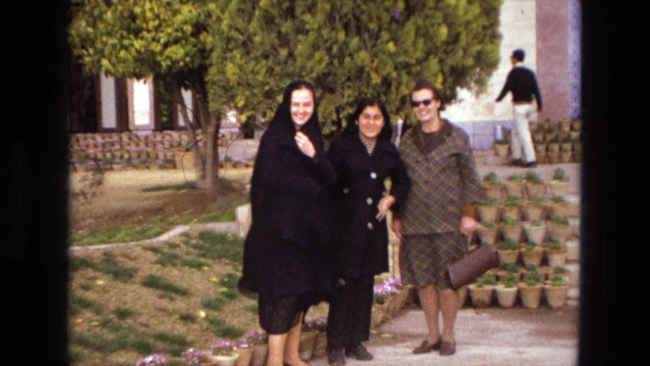 Three women pose in a garden near a building with trees and potted plants.