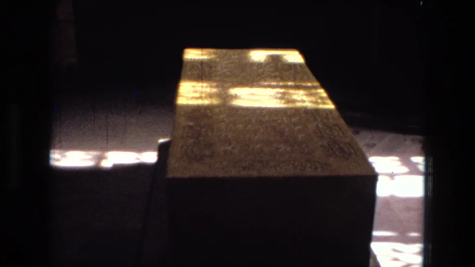 A close view shows a carved stone monument or block in partial shadow, with bright dappled sunlight across its upper surface.