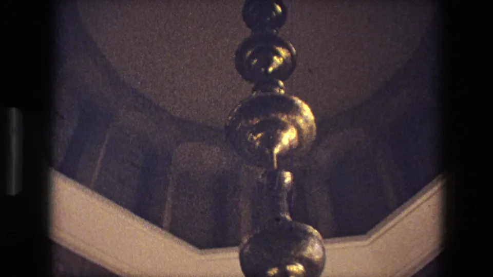 1972 Iran 8mm frame showing a brass chandelier or hanging lamp against a vaulted interior with a pale arch below.